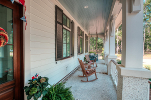 Tabby shell concrete floors with brick accents, operable louvered shutters, Hardie artisan siding, bed-style porch swing, mahogany front door. A front porch with a haint blue v-groove ceiling, tabby concrete floor, black window shutters, white railings, two rocking chairs and a porch swing.