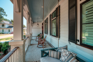 Tabby shell concrete floors with brick accents, operable louvered shutters, Hardie artisan siding, bed-style porch swing, mahogany front door. A front porch with a haint blue v-groove ceiling, tabby concrete floor, black window shutters, white railings, two rocking chairs and a porch swing.