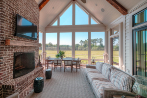 Tabby concrete floors with brick borders, v-groove ceilings, vaulted ceiling, brick fireplace, reclaimed timber mantle. A screened porch with a vaulted ceiling, dining table, striped couch and two end tables, and a TV mounted over a brick fireplace with a reclaimed timber mantle.