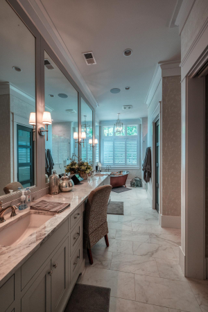 A master bathroom with marble flooring, a copper soaking tub at the far end, and a gray double vanity with a bank of mirrors at the near end.