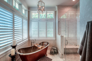 A master bathroom with marble floors, a marble glass-front shower in the far right corner and a copper soaking tub in the far left corner.