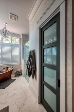 A bathroom with marble floors, a gray paneled water closet door, and a copper soaking tub in one corner.