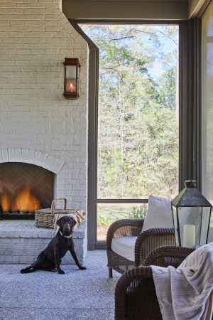 Painted brick outdoor fireplace, tabby shell concrete floor. A chocolate labrador retriever sits in front of a large, floor-to-ceiling white painted brick fireplace in a screened back porch with a tabby shell concrete floor.
