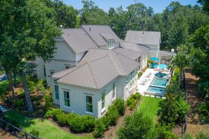 Overhead shot of the pool deck in back of a large white home with a dark metal roof.