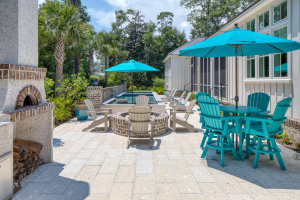 A patio with a swimming pool, wood-fired oven, round brick fire pit, and small round blue dining table and chairs.