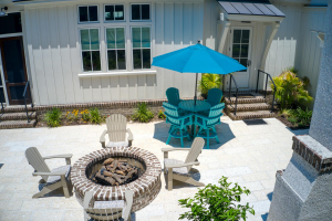 A patio with a swimming pool, wood-fired oven, round brick fire pit, and small round blue dining table and chairs.