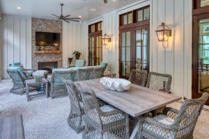Brick fireplace, reclaimed timber mantle, tabby concrete floors, mahogany doors. A screened back porch with a TV mounted over a brick fireplace, a sitting area with wicker furniture, and a dining table with wicker chairs.