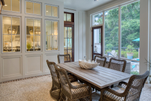 Tabby concrete floors, mahogany doors. A dining table with wicker chairs inside a screened porch with white walls and a tabby concrete floor.