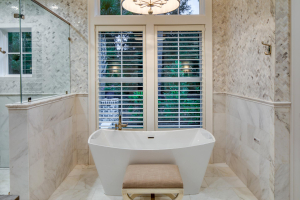 A white free-standing soaker tub sits in an alcove in a master bathroom next to a marble and glass shower.