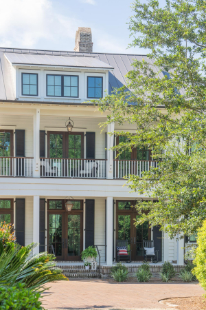 Main house has double porches front and rear, standing seam metal roof, mahogany doors, Bevolo gas lanterns. A large 2-story white house with double porches, standing seam metal roof, bishop's cap chimney topper, and a herringbone pattern paver parking pad.