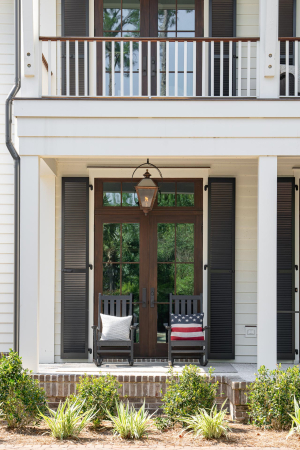 Mahogany doors and Bevolo gas lanterns. Rich brown mahogany double doors on a large home with double porches, white siding, black shutters, and hanging gas lanterns.