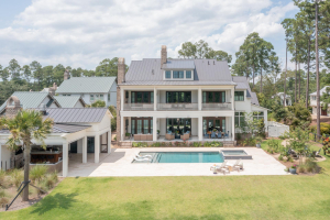A large white home with double porches, pool with a spa, pool house on one end and a fire pit area on the opposite end.