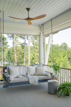 Bed swing, haint blue v-groove ceiling, motorized retractable screens. A blue bed swing with numerous white pillows hangs from a haint blue v-groove ceiling on a second story porch.