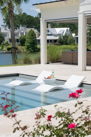 Two curvy white lounge chairs sit partially submerged in shallow end of swimming pool.