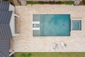 Overhead view looking down on a swimming pool with a spa on one end and two white lounge chairs partially submerged in the opposite shallow end.