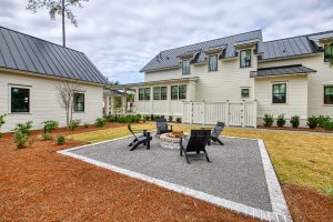 Large two-story white house with a black metal roof, detached carriage house, and a fire pit area.