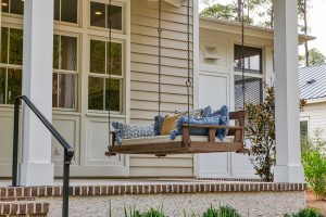 Tabby concrete floor with brick edging, Hardie siding, Marvin windows, and a front porch bed swing. A large wooden bed swing hangs on a covered front porch with tabby concrete floors and beige siding.
