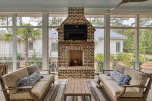"Haint blue" v-groove ceiling, tabby shell concrete floor, seating area with a brick fireplace. A large screened porch with a blue ceiling, white trim, and a tabby shell concrete floor. There is a sitting area with two couches and a coffee table in front of a brick fireplace with a TV mounted above the wooden mantle.
