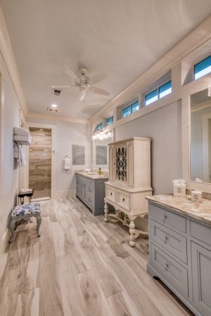 Master bathroom with two gray vanities with marble countertops, wood-pattern tile flooring.