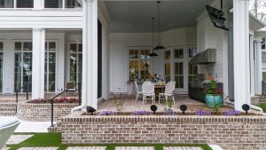 Brick patio, outdoor kitchen, dining area, and motorized porch screens. Outdoor dining and kitchen area of a Palmetto Bluff home built by CS Thomas Construction with brick terrace, stainless grill, and pendant lighting.