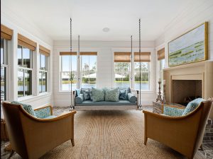 Cast stone fireplace mantle, raised brick hearth, bed swing, and brick flooring. Carolina room overlooking lakefront views in Palmetto Bluff with a suspended daybed swing.