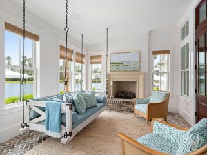 Cast stone fireplace mantle, raised brick hearth, bed swing, and brick flooring. Carolina room interior in Palmetto Bluff with hanging daybed and brick fireplace.