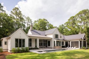 Rear view of luxury Palmetto Bluff home with pool, screened porch, and natural landscape.