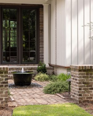 Black fountain bowl framed by brick pillars and native landscaping at the entry of a Palmetto Bluff residence.