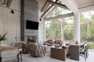 Details: tile-planked fireplace wall, vaulted ceiling, scissor trusses, motorized screen. Screened porch with vaulted ceiling, stone fireplace, and modern outdoor seating.