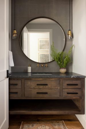 Modern powder room with dark wood vanity, round mirror, and brass fixtures in a Palmetto Bluff home.
