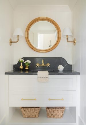 Elegant powder room with black marble vanity, brass fixtures, and round rattan mirror in Bluffton SC home.