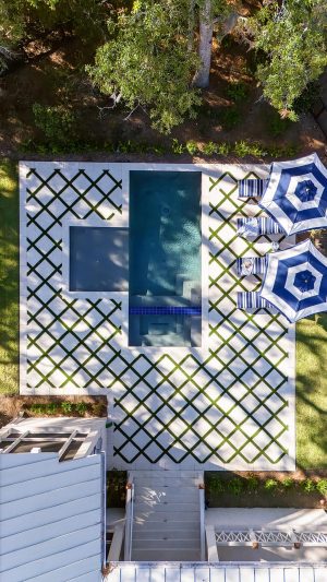 Aerial view of a modern backyard pool and spa with geometric tile design and blue-striped umbrellas in Palmetto Bluff.