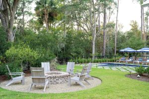 Backyard fire pit surrounded by Adirondack chairs near pool with striped umbrellas in Palmetto Bluff, South Carolina.