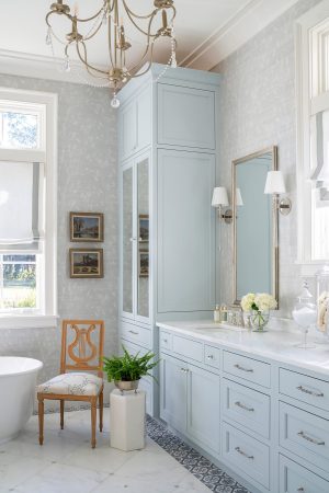 Bathroom with chandelier, marble flooring, and blue cabinetry accented by wall sconces.